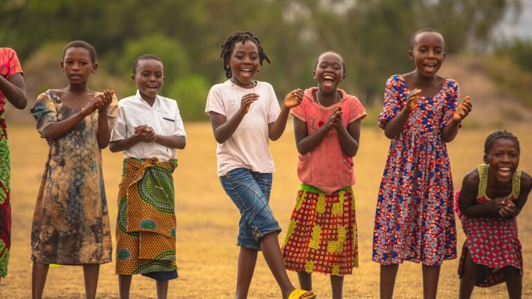 Kinder stehen in einer Reihe nebeneinander und tanzen und klatschen.