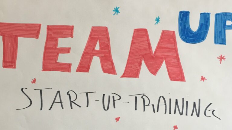 Auf einem Flipchart Papier steht "TeamUp Start Up-Training". Team ist rot, Up ist blau, der Rest ist schwarz. Auf dem Papier sind zudem Sterne gemalt.