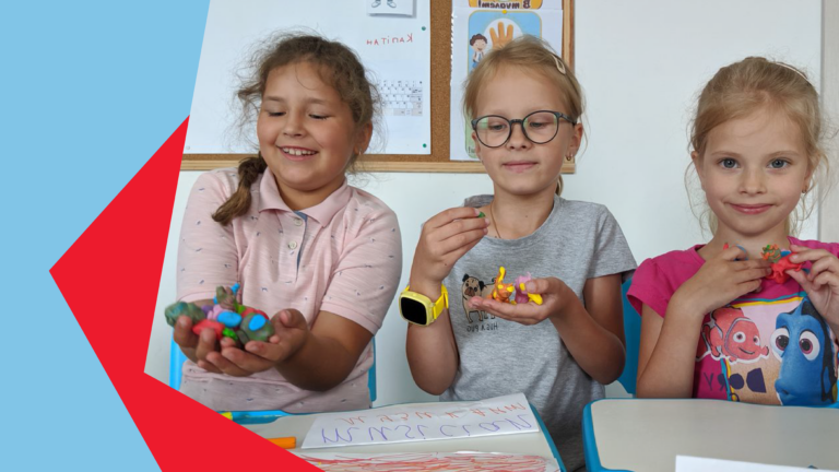 Drei Mädchen sitzen in einem Klassenraum nebeneinaner und haben Spielzeug in der Hand.