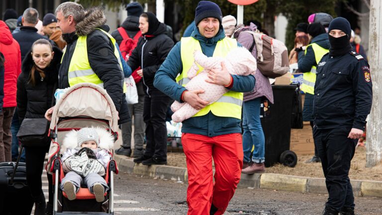 Vielen aufgebrachte Menschen auf einem BIld. Familien und Helfer in Warnwesten. Ein Helfer trägt ein Baby.