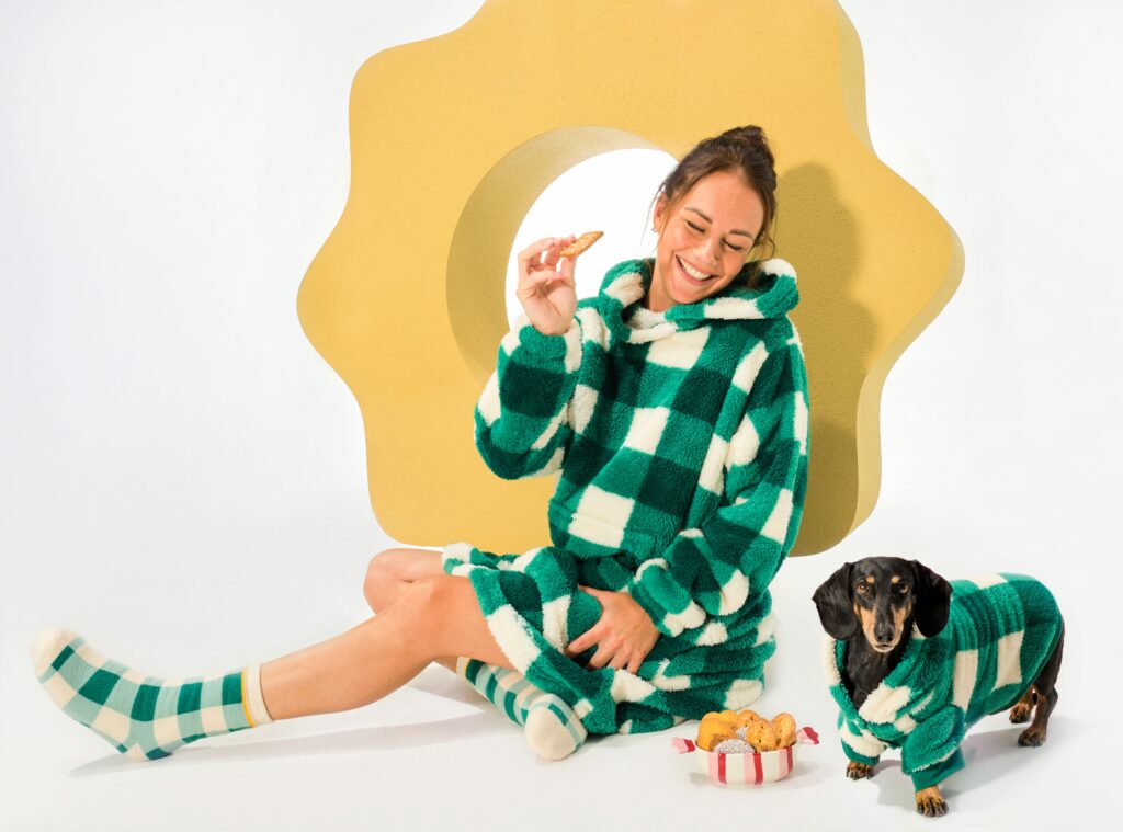 Eine Frau sitzt neben einem Hund. Beide sind mit grün-weiß karierter Homewear bekleidet