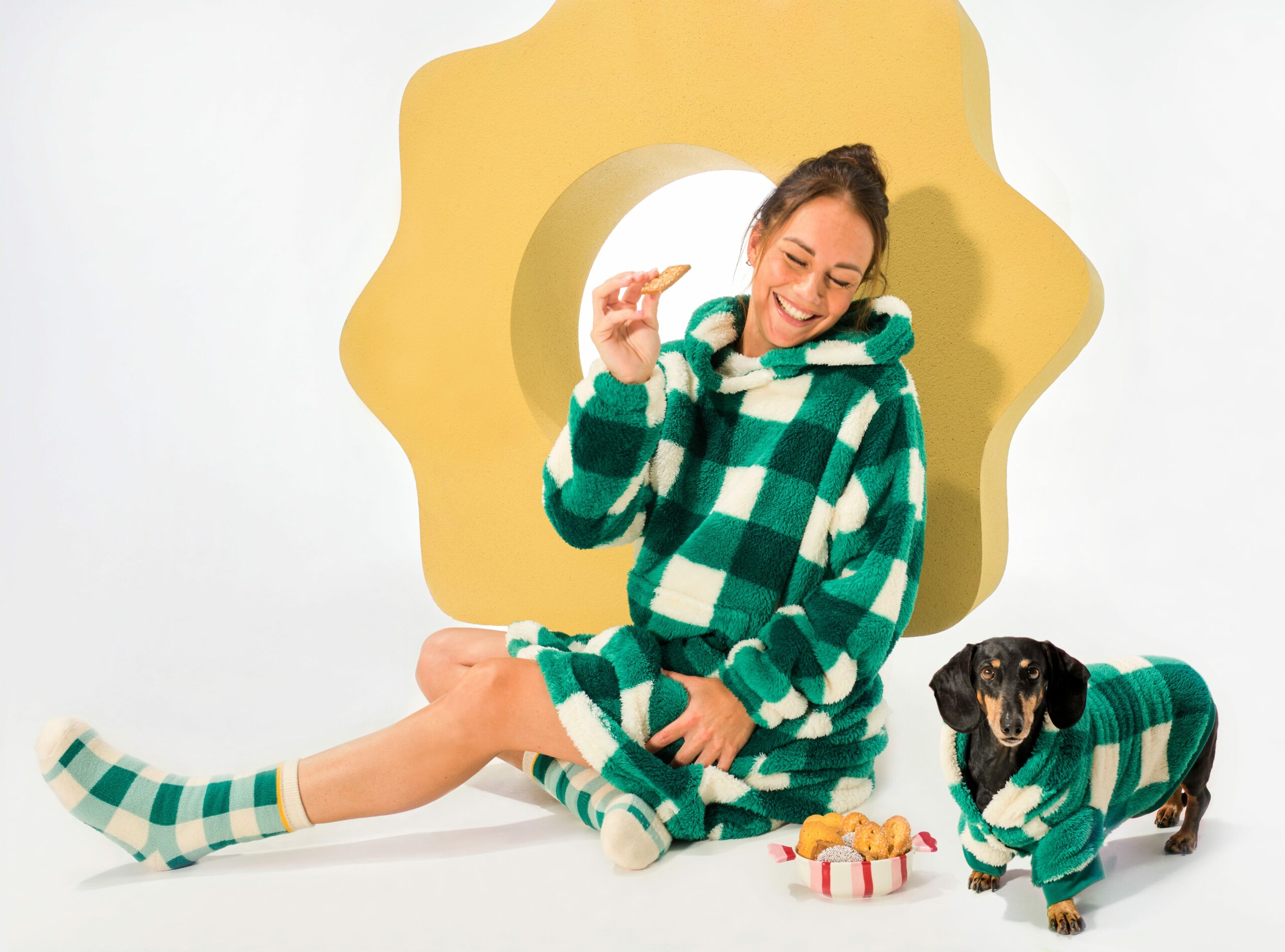 Eine Frau sitzt neben einem Hund. Beide sind mit grün-weiß karierter Homewear bekleidet