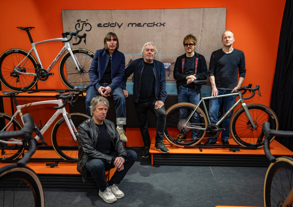 Fünf Mitglieder der Band The Analogues sitzen und stehen in einem Ausstellungsraum mit Fahrrädern.