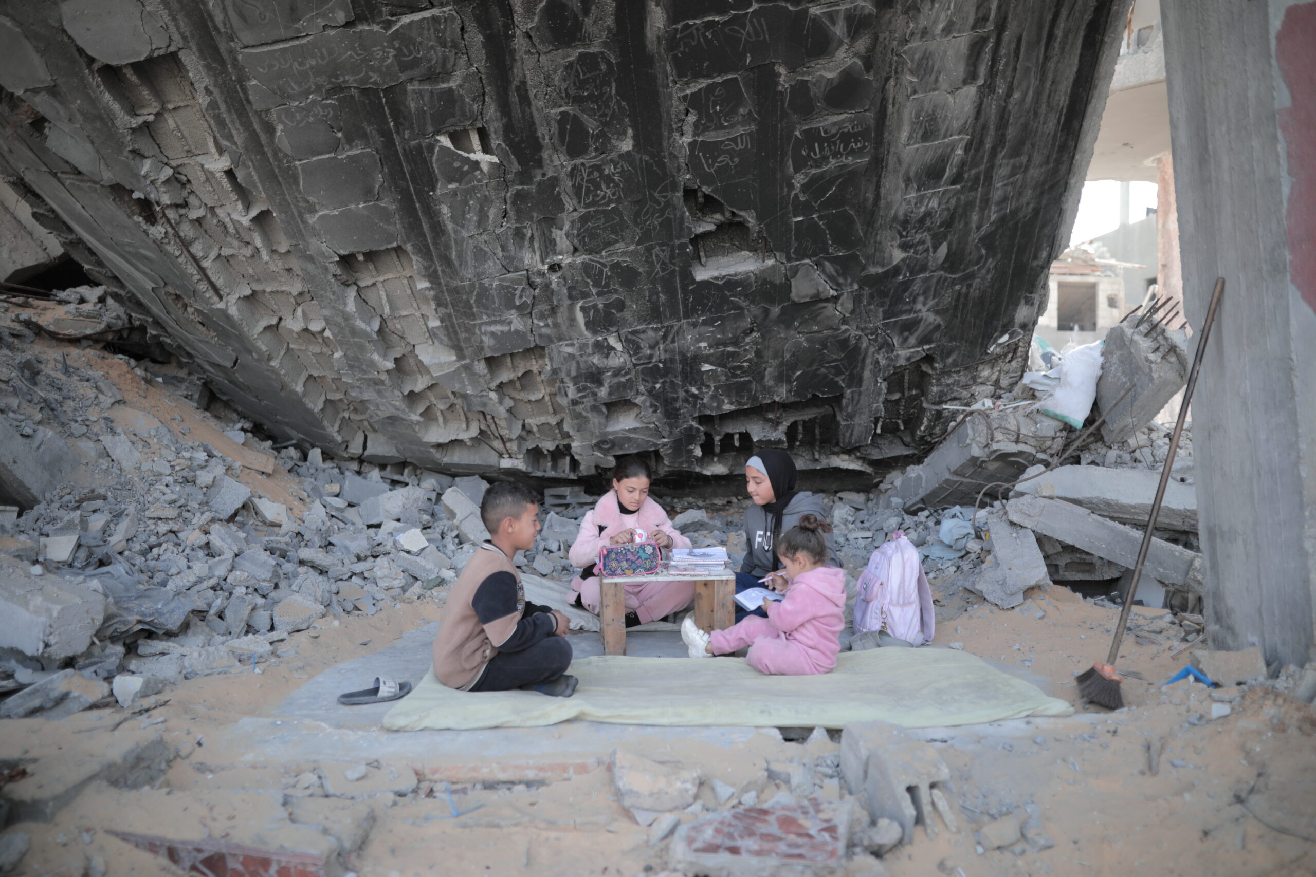 3 Kinder sitzen inmitten von Trümmern auf einer Decke