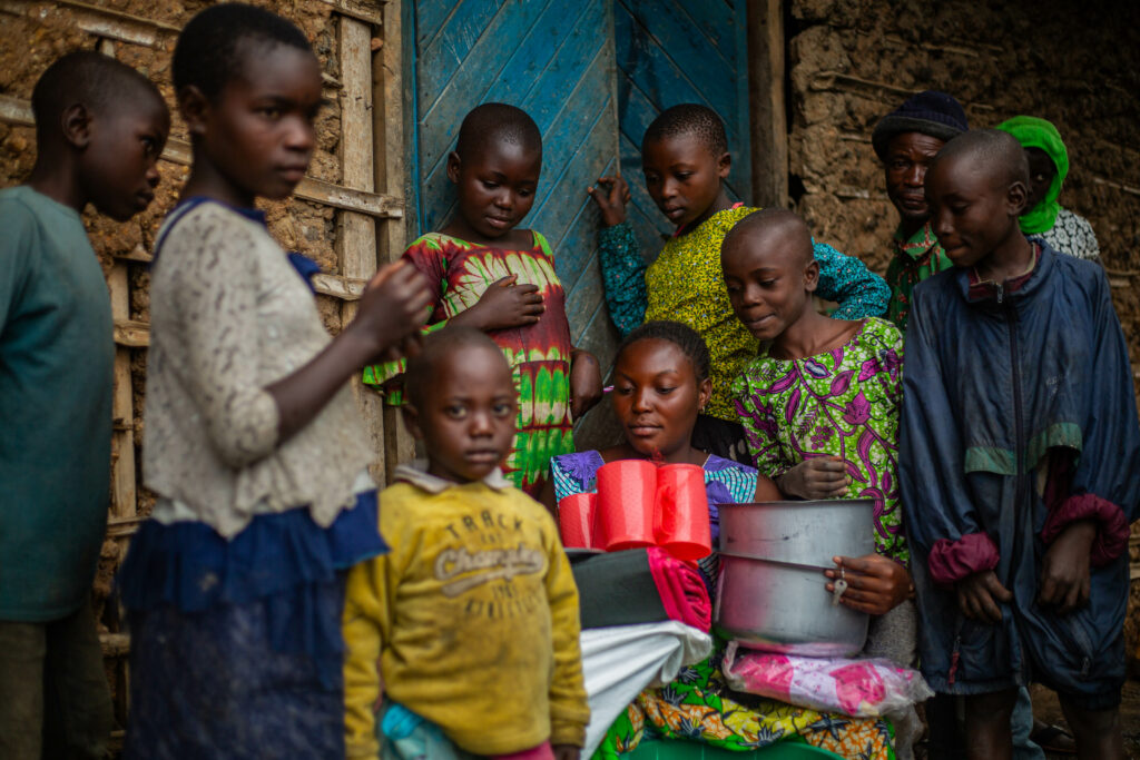 Kinder stehen um eine Frau Herum die einen Kochtopf hält